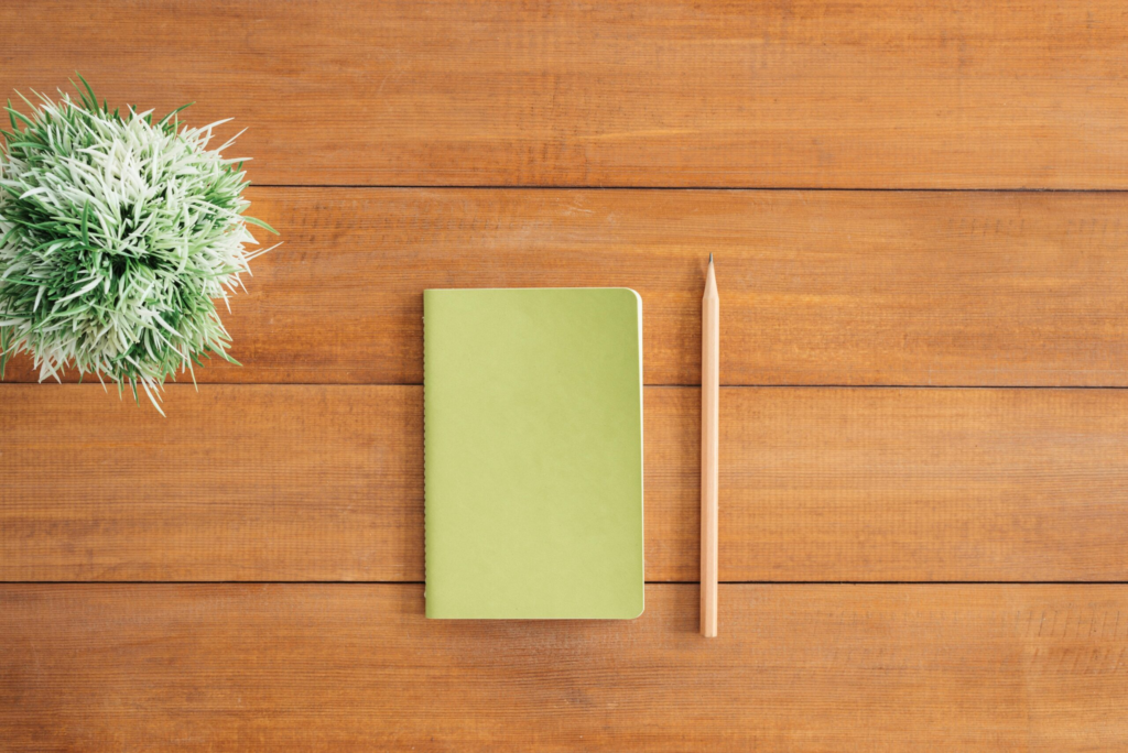 pexels-photo-733854-733854 Flat lay of green notebook and pencil on wooden desk with plant. Perfect for creativity and organization themes.